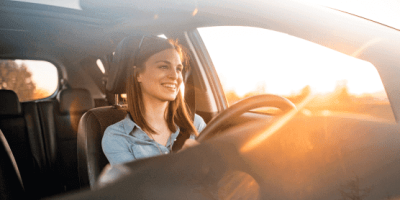 Een vrolijke vrouw die aan het lachen is terwijl zij aan het rijden is met de zonstralen door haar ruit.