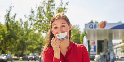 Une femme avec une carte d'épargne Q8 smiles devant sa bouche. 